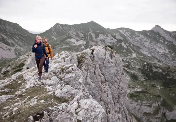 Zwei Wanderer genießen eine 5-tägige Tour durch die Alpen. Sie gehen auf einem felsigen Grat mit beeindruckender Bergkulisse.