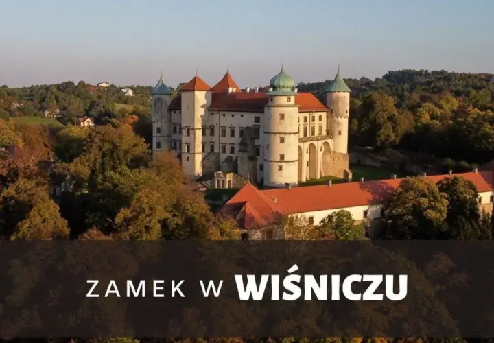 Majestatyczny zamek Wiśnicz otoczony jesiennymi drzewami, z charakterystycznymi wieżami i czerwonymi dachami.