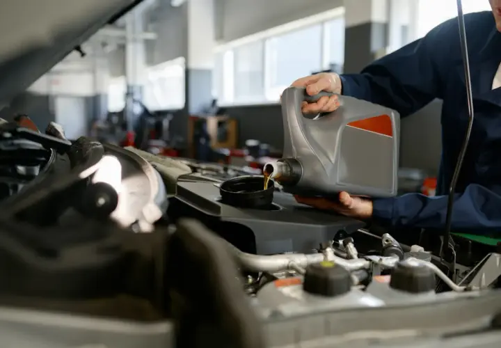 Mechanik wylewa olej do silnika. Zastanawiasz się, ile kosztuje wymiana oleju w silniku?