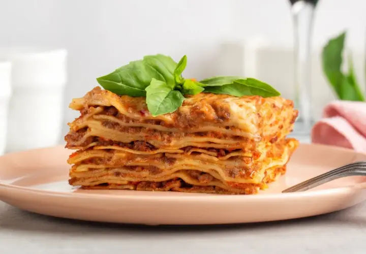 Pyszna, wielowarstwowa lasagne z mięsnym sosem i serem, udekorowana bazylią. Idealny przepis na obiad.