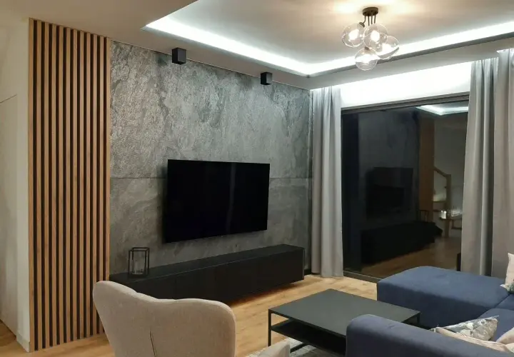 Nowoczesny salon z betonem architektonicznym, który świetnie komponuje się z drewnianymi lamelami i granatową sofą.