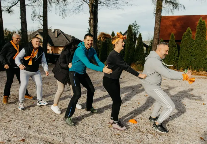 Grupa ludzi w pomarańczowych szalikach bierze udział w ćwiczeniu integracyjnym na zewnątrz.