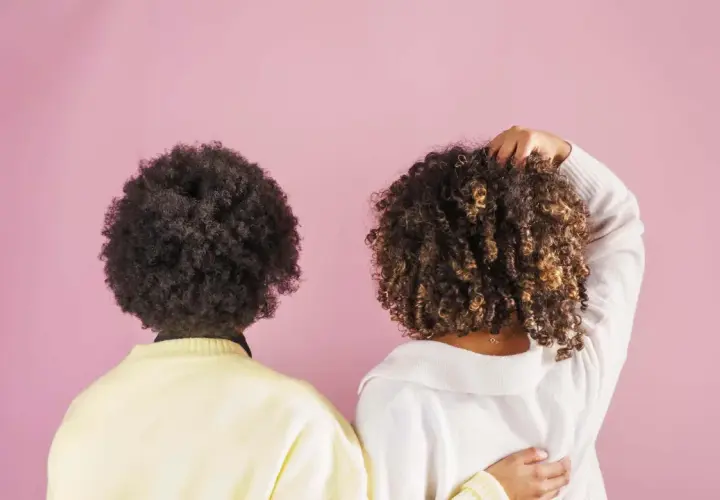 Dos personas con cabello rizado, una con afro oscuro y otra con rizos castaños, muestran la belleza natural de su cabello, quizás inspiradas por el método no poo.