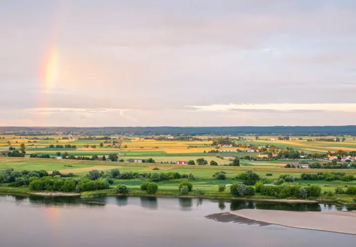 Krajobraz Kociewia nad rzeką, pola uprawne, domy i tęcza na niebie.