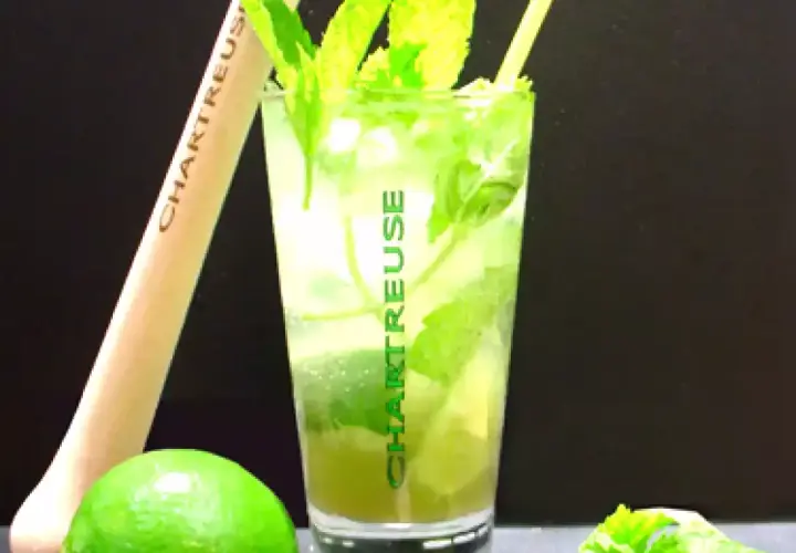 Un verre de cocktail Chartreuse, garni de menthe fraîche et de citron vert, prêt à être dégusté.