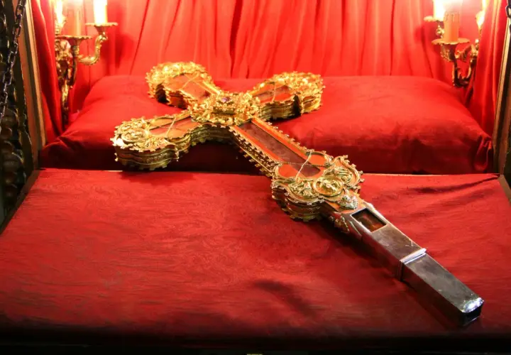 Cruz de Caravaca dorada y enjoyada, expuesta sobre terciopelo rojo en el monasterio de Santo Toribio de Liébana.
