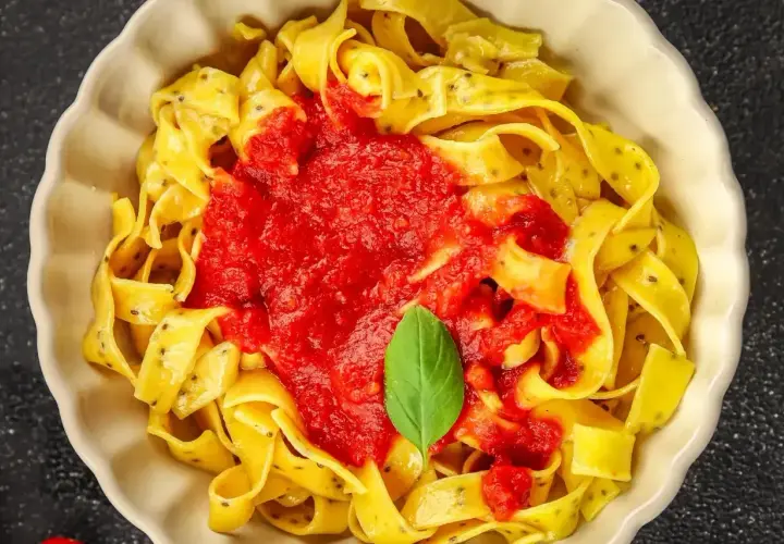 Pyszne fettuccine i tagliatelle z sosem pomidorowym i listkiem bazylii w białej misce.
