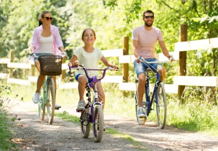 Rodzina cieszy się rodzinną wycieczką rowerową po malowniczych Mazurach. Uśmiechnięta dziewczynka na rowerze, mama i tata jadą leśną ścieżką.