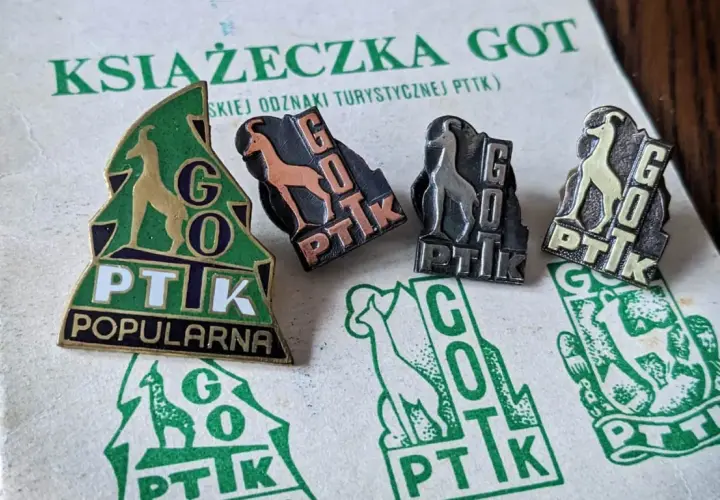 Książeczka GOT z odznakami turystycznymi PTTK. Widoczne cztery odznaki z kozicą i napisem GOT PTTK w różnych kolorach.