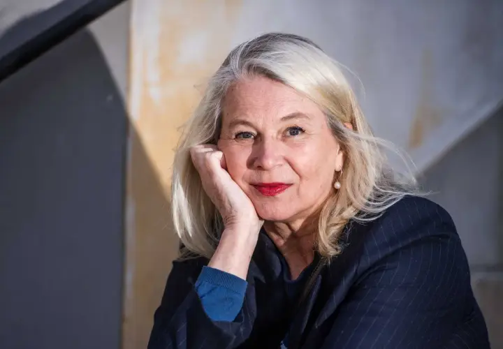 Helena von Zweigbergk, med sin partner vid sin sida, ler mot kameran. Hennes blonda hår ramar in ett ansikte med röda läppar och en pärlörhänge.