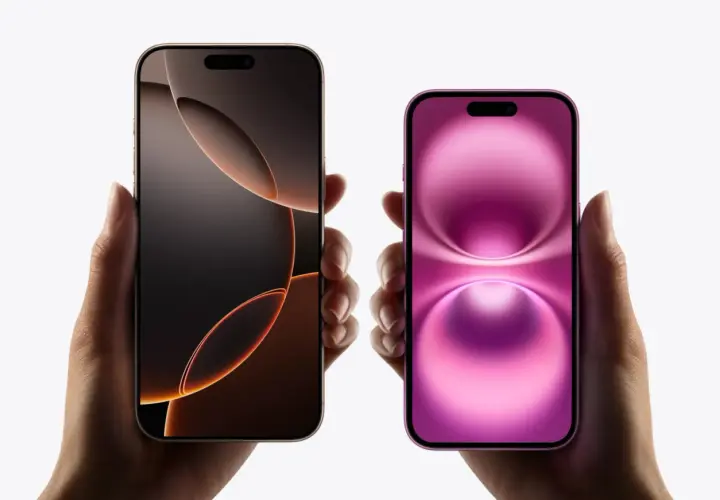 Dwie dłonie trzymają dwa iPhone'y. Jeden ma ciemny ekran z pomarańczowymi akcentami, drugi różowy. Oba modele mają dynamiczną wyspę.