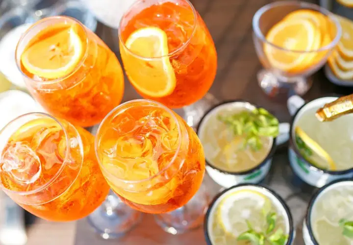 Orzeźwiający drink z prosecco, udekorowany plasterkiem pomarańczy, czeka na spróbowanie. Obok inne napoje z cytryną i miętą.