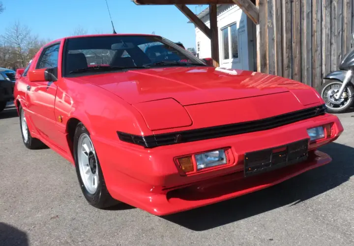 Czerwony Mitsubishi Starion z lat 80. błyszczy w słońcu. Klasyk sportowy z wysuwanymi światłami.