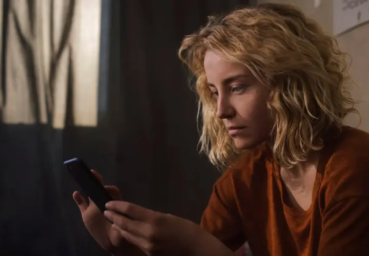Zamyślona dziewczyna z blond włosami trzyma telefon, czekając na wiadomość. Może ta dziewczyna nie odpisuje.