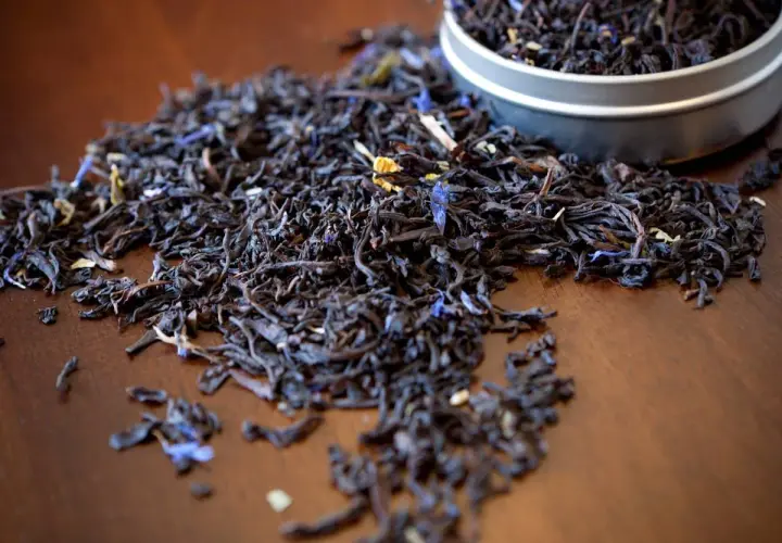 Garść liści aromatycznej herbaty earl grey, z niebieskimi płatkami chabru, rozsypana na drewnianym blacie.