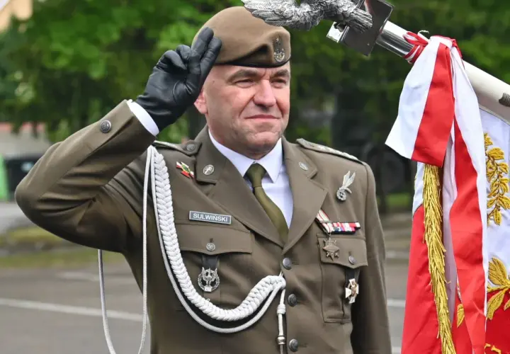 Pułkownik Suliwiński w mundurze salutuje obok polskiej flagi.