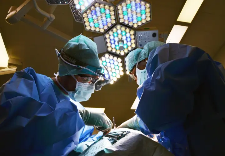 Chirurdzy w sterylnych strojach pracują pod jasnym światłem lampy operacyjnej. Po zabiegu mogą wystąpić narkoza skutki uboczne.
