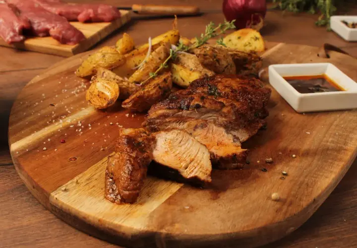 Pluma de porc recette : viande grillée juteuse, pommes de terre rôties et sauce savoureuse sur une planche en bois.