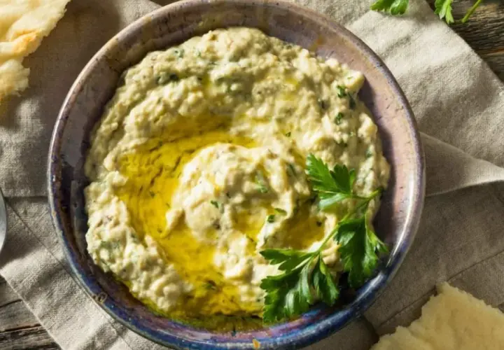 Baba ganush cremoso en un cuenco, con aceite de oliva y perejil fresco. Pan de pita al lado.