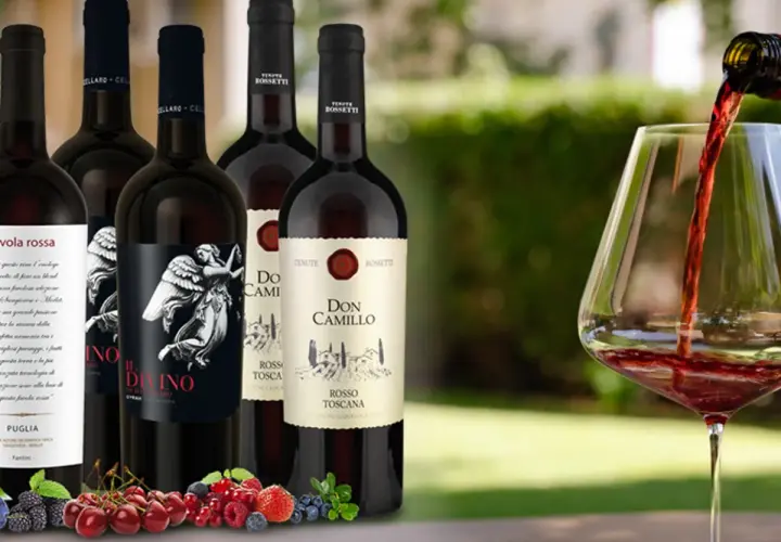 Flaschen mit teurem italienischem Rotwein, darunter "Il Divino" und "Don Camillo", werden vor einem Glas Rotwein präsentiert, in das gerade eingeschenkt wird. Frische Beeren und Kirschen liegen im Vordergrund.