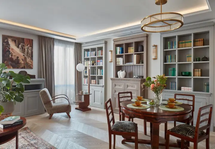 Eleganckie wnętrze w stylu klasycznym. Okrągły stół z krzesłami, regały z książkami, obraz i wygodny fotel tworzą przytulną atmosferę.