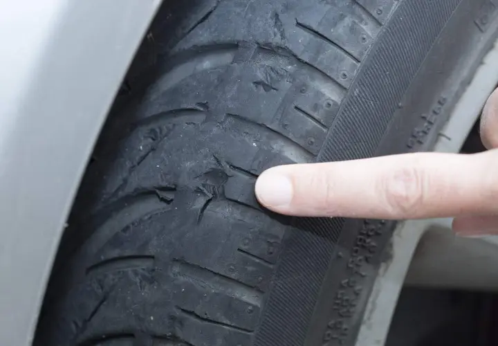 Dedo señala el desgaste de ruedas delanteras por el interior, mostrando daños severos en el caucho.