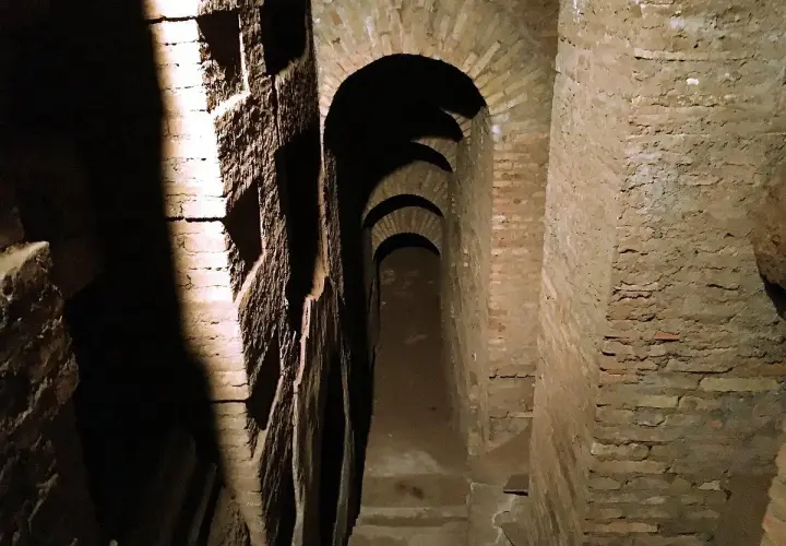 Passage voûté dans les catacombes de Rome, avec des niches creusées dans le mur de briques.