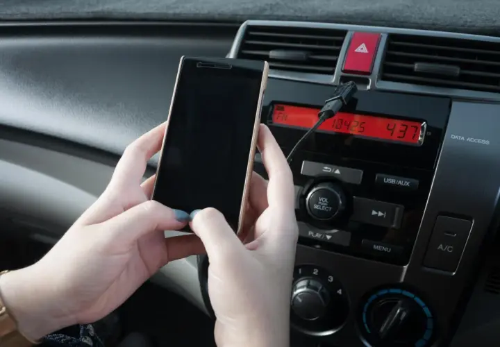 Ręce trzymają telefon, który jest podłączony kablem do radia samochodowego. Prosty sposób, jak połączyć telefon z samochodem.