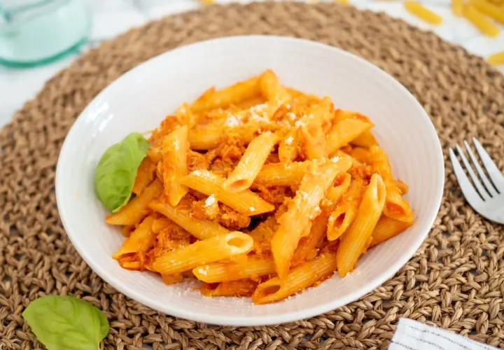 Un plato de macarrones con atún, cubiertos con salsa de tomate y queso rallado, adornado con hojas de albahaca fresca.