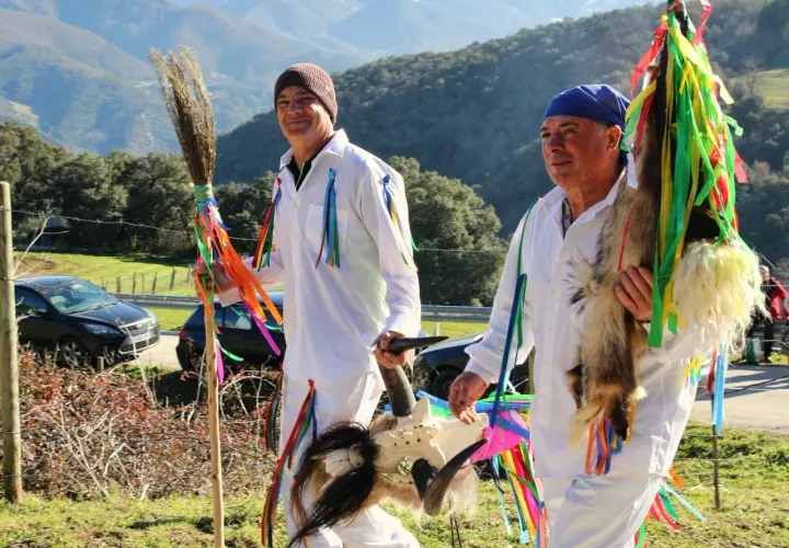 Hombres con trajes blancos y cintas de colores, portando una escoba y una cabeza de cabra, celebran tradiciones de Cantabria.