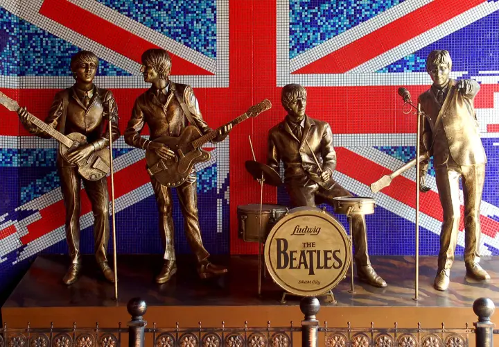 Brązowe posągi **The Beatles** grające na tle mozaikowej flagi Wielkiej Brytanii.