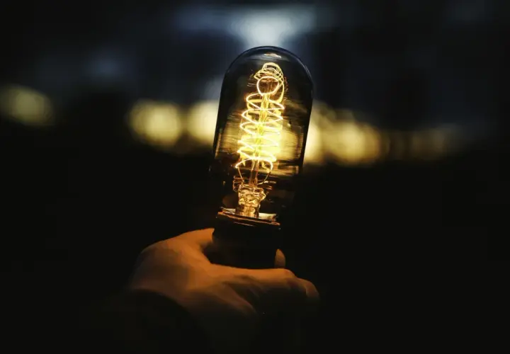 Dłoń trzyma żarzącą się żarówkę Edisona. Zastanawiasz się, ile to wat, gdy świeci 806 lumenów?