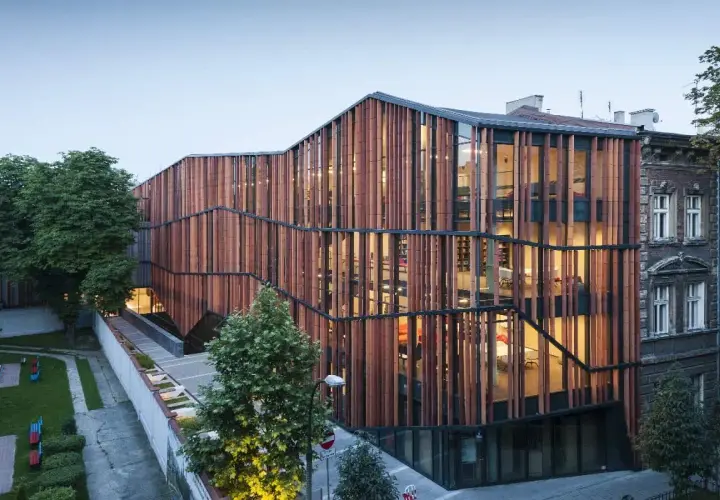 Nowoczesna architektura Małopolskiego Ogrodu Sztuki w Krakowie, z drewnianą fasadą i przeszklonymi wnętrzami, tworzy rajską oazę dla kultury.