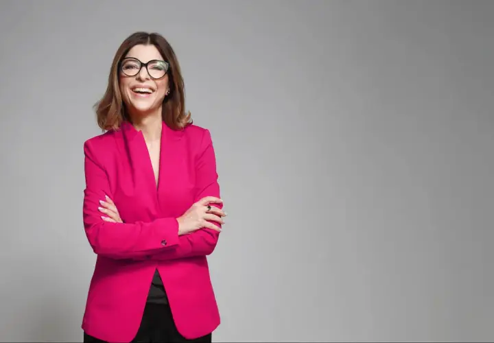 Uśmiechnięta kobieta w różowym żakiecie i okularach, prezentująca styl business formal.