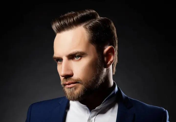 Ein Mann mit Bart und einem eleganten Seitenscheitel, gekleidet in einem blauen Anzug.