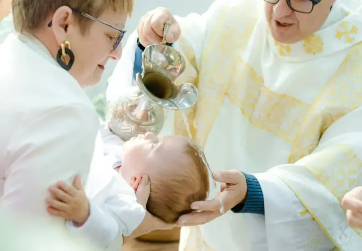 Chrzest dziecka. Kapłan polewa główkę niemowlęcia wodą święconą. Warto wiedzieć, ile kosztuje chrzest, by odpowiednio się przygotować.
