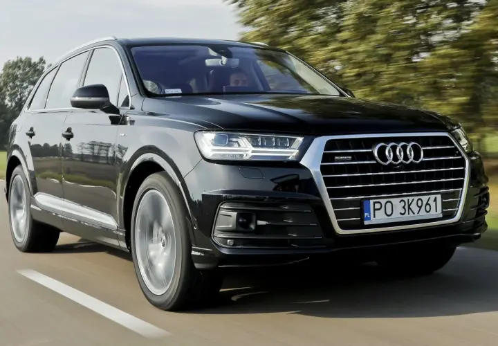 Czarny Audi Q7 3.0 TDI pędzi po drodze, otoczony zielenią drzew.