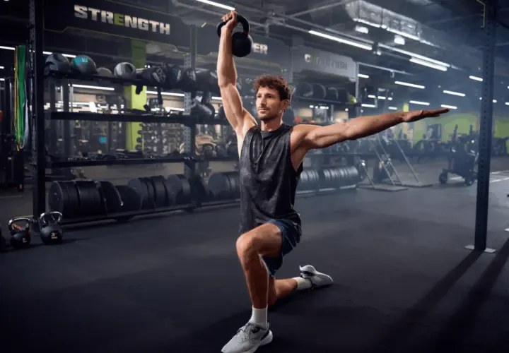 Mężczyzna wykonuje ćwiczenie z kettlebell w siłowni. To część jego zajęć tbc.