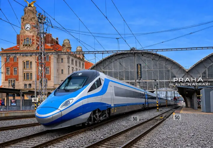 Nowoczesne oznaczenie Pendolino na tle zabytkowego dworca w Pradze. Pociąg w kolorach niebieskim i srebrnym stoi na torach.