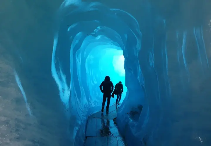 Dwie sylwetki wędrują przez lodowy tunel. Jasne, turkusowe światło przebija się z głębi, tworząc magiczną atmosferę. To jak podróż do wnętrza lodowca, gdzie czas się zatrzymał, a jedynym dźwiękiem jest echo kroków.