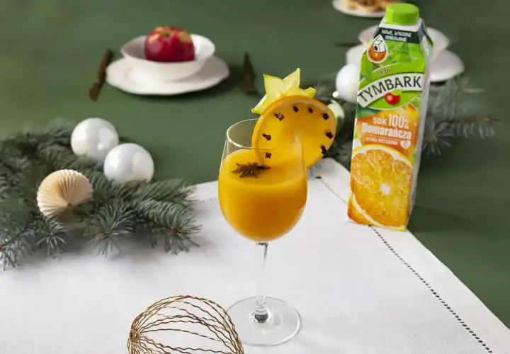 Aromatyczny likier pomarańczowy z goździkami i anyżem, ozdobiony plasterkiem pomarańczy i gwiazdką. Obok karton soku pomarańczowego.