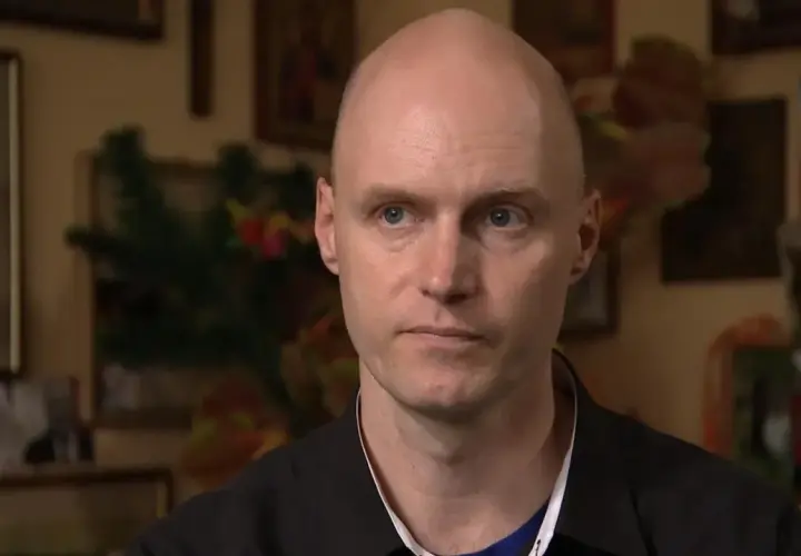 Krzysztof Igor Krawczyk, łysy mężczyzna z niebieskimi oczami, w czarnej koszuli, na tle rodzinnych zdjęć.