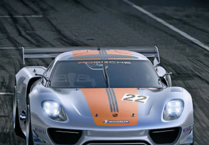 Srebrny Porsche 918 Spyder z pomarańczowymi pasami i numerem 22 na masce pędzi po torze wyścigowym.