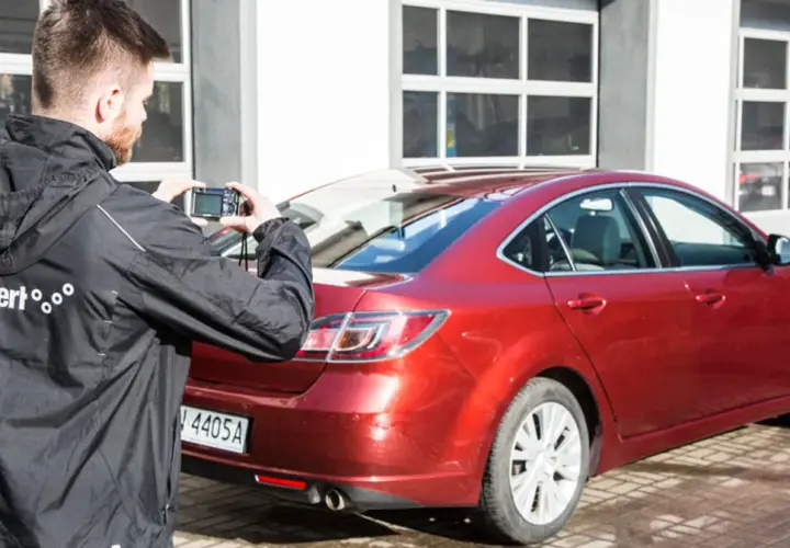 Mężczyzna robi zdjęcie czerwonego samochodu, który jest na sprzedaż bezpośrednio od właściciela.