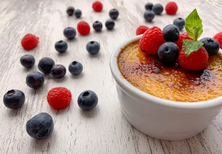 Creme brulee rezept: Ein cremiges Dessert mit karamellisierter Zuckerkruste, garniert mit frischen Beeren und Minze.