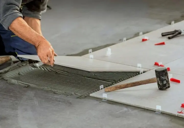 Pose de carrelage mal posé, avec de la colle visible et des cales rouges. Un marteau repose sur une des dalles.