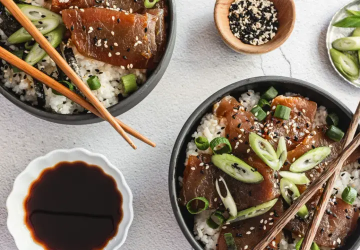 Two bowls of delicious tuna rice don, garnished with sesame seeds and green onions, are ready to be enjoyed with chopsticks.