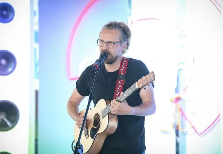 Mężczyzna w okularach gra na gitarze i śpiewa do mikrofonu. Chciałbyś, żeby ktoś powiedział mu "weź się przytul".