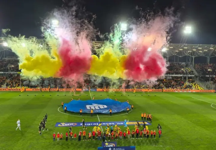 Oprawa meczu Korona Kielce – Jagiellonia Białystok. Piłkarze wychodzą na murawę w otoczeniu gęstego dymu w barwach żółto-czerwonych.