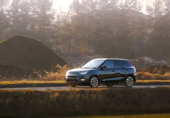 Czarny hatchback jedzie drogą wśród jesiennych wzgórz i drzew.